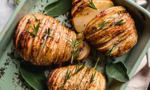 Pommes de terre Hasselback dorées et croustillantes, garnies de romarin frais et d'herbes, dans un plat vert.