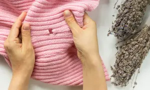 Mains examinant un pull rose troué, vestige d'un cocon de mite textile, à côté de bouquets de lavande séchée.