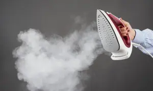 Une main tient un fer à repasser qui émet de la vapeur, suggérant l'action de détartrer le fer à repasser pour un entretien optimal.