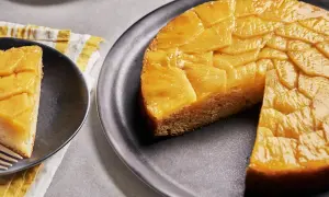 Un délicieux gâteau ananas renversé, avec une tranche servie sur une assiette noire. Les fruits caramélisés brillent sous la lumière.