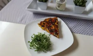 Tranche de tarte aux poivrons colorée, servie avec une salade de pousses fraîches sur une assiette blanche.