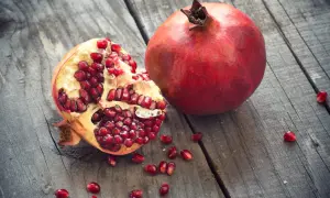 Une grenade entière et une ouverte, révélant ses arilles rouges éclatantes, sur un fond de bois vieilli. Un délice de la grenade fruit saison.