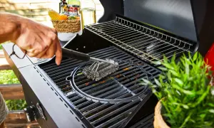 Main d'homme nettoyant une grille de barbecue avec une brosse métallique. Préparation pour la prochaine cuisson.