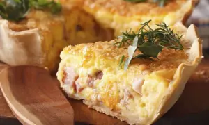 Une tranche de véritable quiche lorraine, garnie d'herbes fraîches, sur une planche en bois avec une cuillère.
