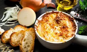 Une délicieuse soupe à l'oignon gratinée, servie avec des croûtons croustillants et du fromage fondu. Les ingrédients frais, comme les oignons et l'ail, sont disposés autour du plat.