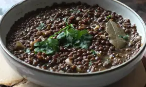 Un plat de lentilles vertes mijotées, garni de persil frais et d'une feuille de laurier. Parfait pour des recettes de lentilles vertes réconfortantes.