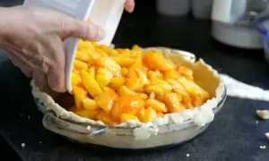 Une main verse des morceaux de pêches en boîte dans une tarte.
