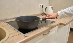 Une main tient une poêle sur une plaque de cuisson vitrocéramique, illustrant la différence entre plaque électrique et induction.