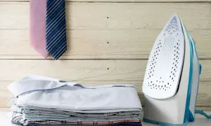 Fer à repasser prêt à l'emploi, avec une pile de chemises et deux cravates. La température idéale pour un repassage impeccable.
