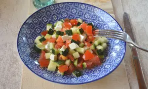 Salade de courgettes à la grecque, fraîche et colorée, avec des dés de tomates, courgettes et feta dans une assiette bleue.