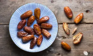 Assiette de dattes, un fruit en d. Ces fruits secs, brillants et caramélisés, sont disposés sur une assiette bleue et blanche et sur une table en bois rustique.