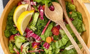 Salade verte fraîche et colorée, parfaite pour une recette légère. Radis, concombre, tomates cerises et citron dans un saladier en bois avec des couverts.