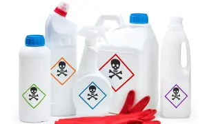 Plusieurs produits ménagers blancs, dont un pulvérisateur, portent un pictogramme toxique. Des gants rouges sont posés devant.