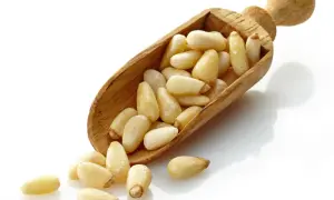 Une cuillère en bois déborde de pignons de pin, quelques-uns roulent sur le fond blanc.