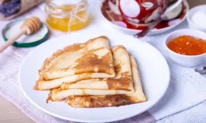 Pile de crêpes dorées, prêtes pour la préparation de la pâte à crêpes. Accompagnées de miel, confiture et d'une tasse de thé.