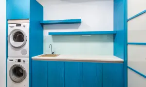 Espace buanderie moderne avec lave-linge et sèche-linge superposés, évier et placards bleus.