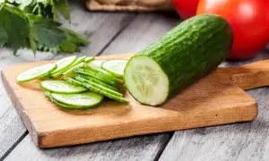Un concombre entier et des rondelles sur une planche à découper. La question "faut il eplucher un concombre" se pose devant cette image fraîche.