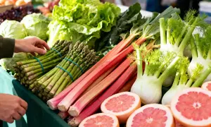 Un étal de marché débordant de fruits et légumes de saison : asperges, rhubarbe, fenouils, laitues et pamplemousses coupés.