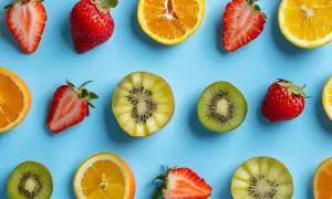 Fraises, kiwis et oranges coupés en deux, disposés en rangées sur un fond bleu. Un assortiment de fruit en p.