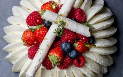 Pavlova aux fruits rouges, décorée de meringues fines et de feuilles d'or. Un délice visuel et gustatif.