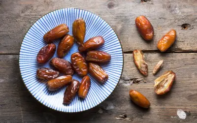 Assiette de dattes, un fruit en d. Ces fruits secs, brillants et caramélisés, sont disposés sur une assiette bleue et blanche et sur une table en bois rustique.