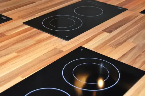 Plaques de cuisson modernes sur un plan de travail en bois. L'une est une plaque à induction ou vitrocéramique avec des cercles blancs.
