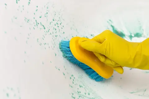Main jaune, brosse bleue frottant une tache impossible à enlever sur une surface blanche.