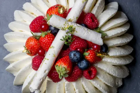 Pavlova aux fruits rouges, décorée de meringues fines et de feuilles d'or. Un délice visuel et gustatif.