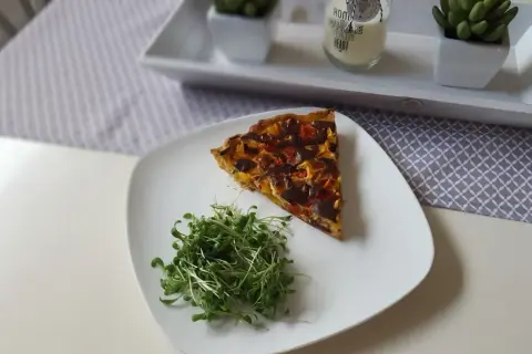 Tranche de tarte aux poivrons colorée, servie avec une salade de pousses fraîches sur une assiette blanche.