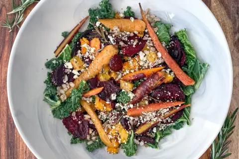 Salade composée colorée avec carottes rôties, betteraves, chou frisé et fromage émietté, garnie de romarin frais.
