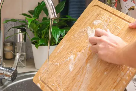 Nettoyer une planche à découper en bois avec du bicarbonate de soude et de l'eau savonneuse sous le robinet.