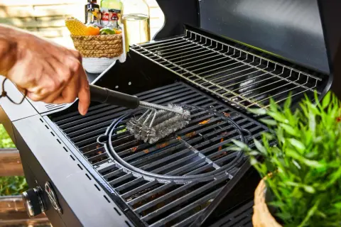 Main d'homme nettoyant une grille de barbecue avec une brosse métallique. Préparation pour la prochaine cuisson.