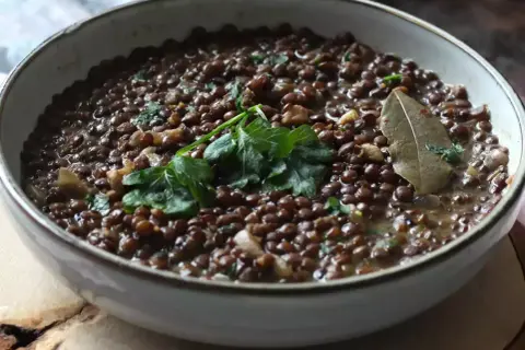 Un plat de lentilles vertes mijotées, garni de persil frais et d'une feuille de laurier. Parfait pour des recettes de lentilles vertes réconfortantes.