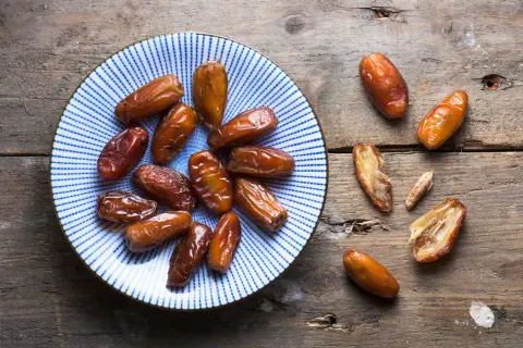 Assiette de dattes, un fruit en d. Ces fruits secs, brillants et caramélisés, sont disposés sur une assiette bleue et blanche et sur une table en bois rustique.