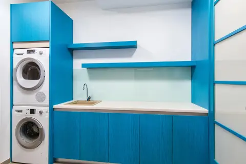 Espace buanderie moderne avec lave-linge et sèche-linge superposés, évier et placards bleus.
