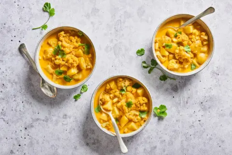 Trois bols de chou-fleur curry crémeux, garni de coriandre fraîche. Un plat réconfortant et savoureux.
