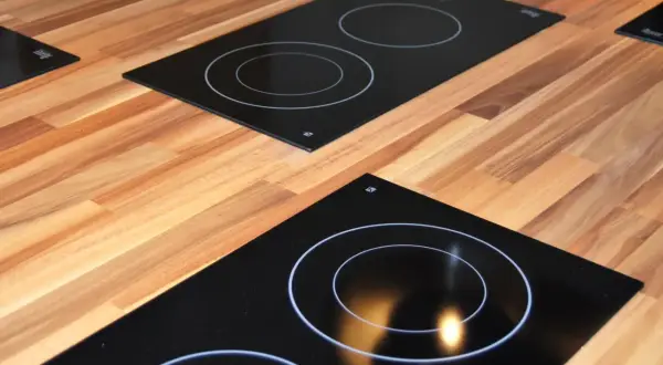 Plaques de cuisson modernes sur un plan de travail en bois. L'une est une plaque à induction ou vitrocéramique avec des cercles blancs.