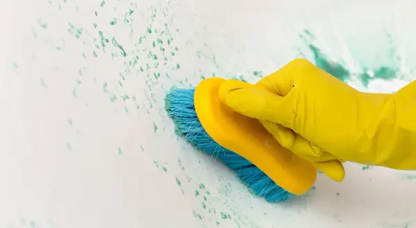 Main jaune, brosse bleue frottant une tache impossible à enlever sur une surface blanche.