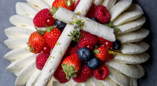 Pavlova aux fruits rouges, décorée de meringues fines et de feuilles d'or. Un délice visuel et gustatif.