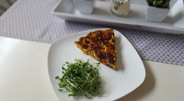 Tranche de tarte aux poivrons colorée, servie avec une salade de pousses fraîches sur une assiette blanche.