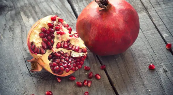 Une grenade entière et une ouverte, révélant ses arilles rouges éclatantes, sur un fond de bois vieilli. Un délice de la grenade fruit saison.