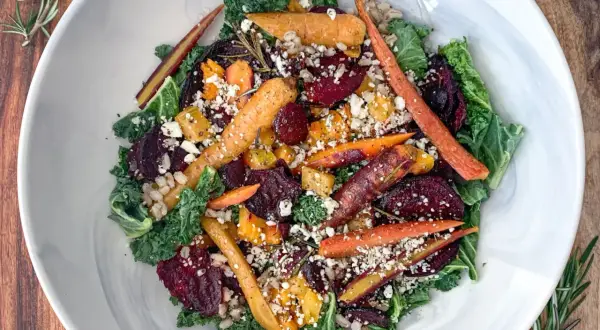 Salade composée colorée avec carottes rôties, betteraves, chou frisé et fromage émietté, garnie de romarin frais.