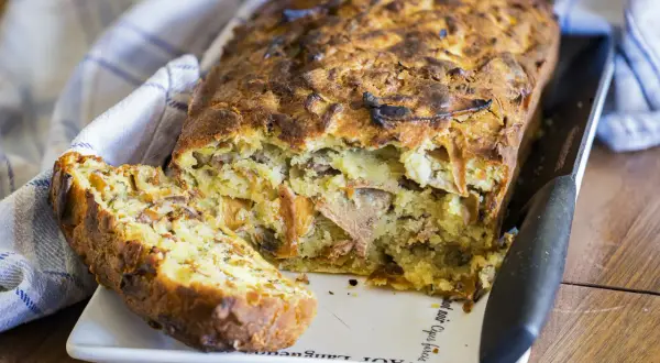 Un cake aux fanes de carottes, doré et moelleux, avec une tranche coupée, prêt à être dégusté.