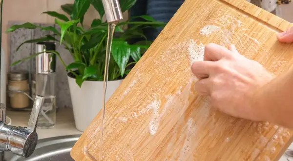Nettoyer une planche à découper en bois avec du bicarbonate de soude et de l'eau savonneuse sous le robinet.