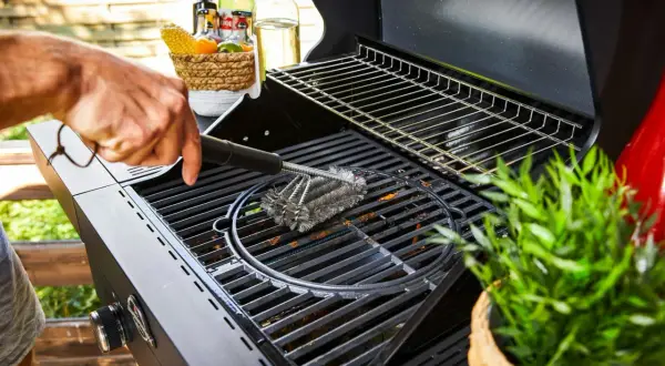 Main d'homme nettoyant une grille de barbecue avec une brosse métallique. Préparation pour la prochaine cuisson.