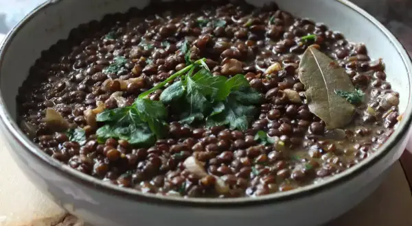 Un plat de lentilles vertes mijotées, garni de persil frais et d'une feuille de laurier. Parfait pour des recettes de lentilles vertes réconfortantes.
