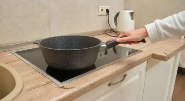 Une main tient une poêle sur une plaque de cuisson vitrocéramique, illustrant la différence entre plaque électrique et induction.