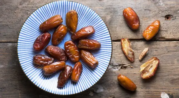 Assiette de dattes, un fruit en d. Ces fruits secs, brillants et caramélisés, sont disposés sur une assiette bleue et blanche et sur une table en bois rustique.