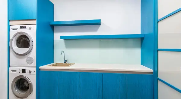 Espace buanderie moderne avec lave-linge et sèche-linge superposés, évier et placards bleus.