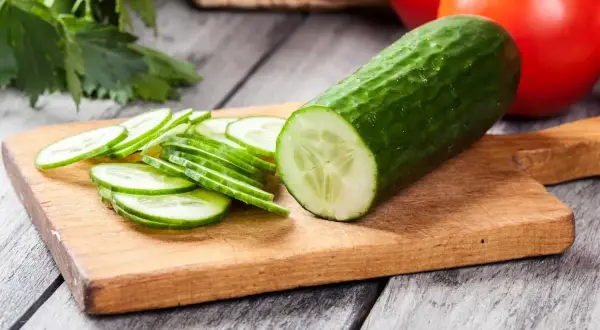 Un concombre entier et des rondelles sur une planche à découper. La question "faut il eplucher un concombre" se pose devant cette image fraîche.